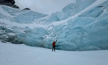 Persona de pie sobre la laguna congelada del Glaciar Ojo del Albino en Ushuaia, levantando la mano frente a las imponentes paredes de hielo.