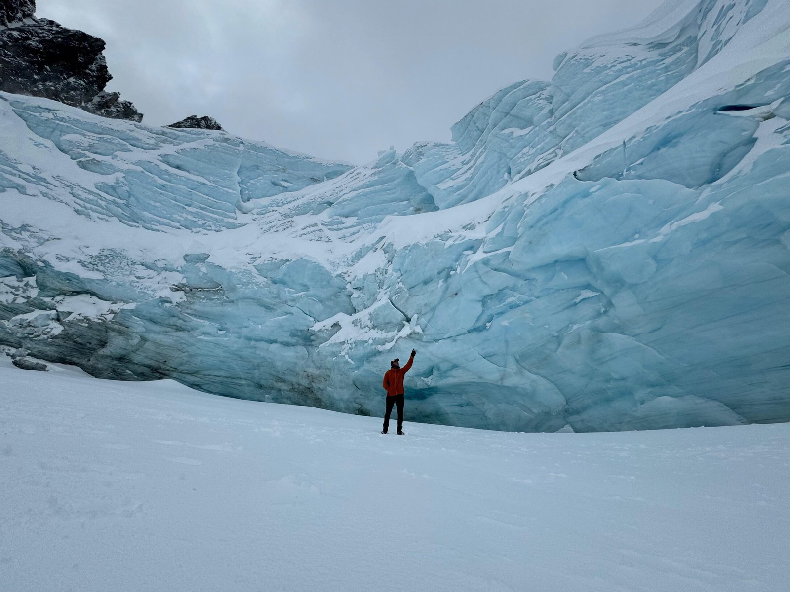 Persona de pie sobre la laguna congelada del Glaciar Ojo del Albino en Ushuaia, levantando la mano frente a las imponentes paredes de hielo.