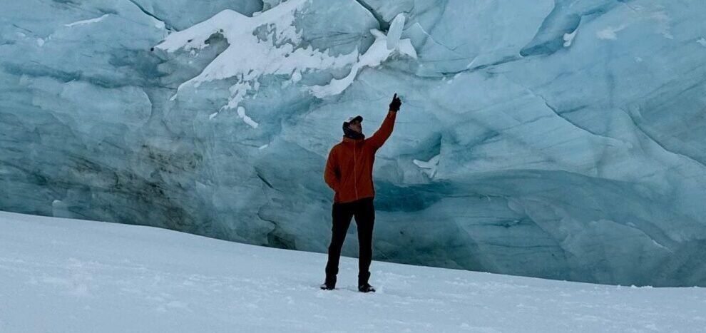 Persona de pie sobre la laguna congelada del Glaciar Ojo del Albino en Ushuaia, levantando la mano frente a las imponentes paredes de hielo.
