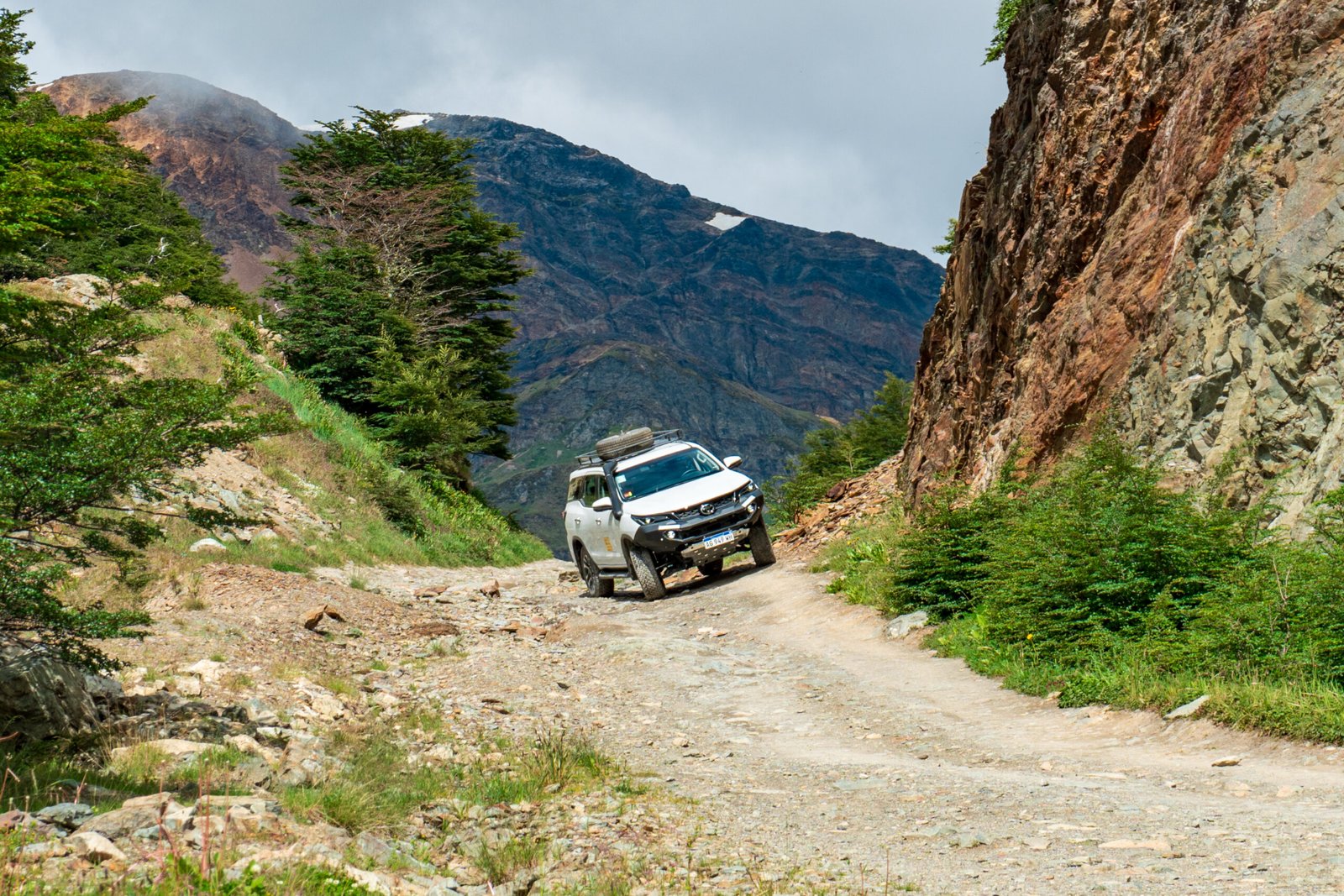 Camioneta 4x4 avanzando por un camino de montaña rocoso en Tierra del Fuego rodeado de naturaleza y montañas.