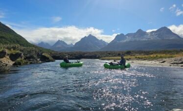 Personas practicando packrafting en el Río Olivia con montañas de los Andes Fueguinos al fondo en Ushuaia.