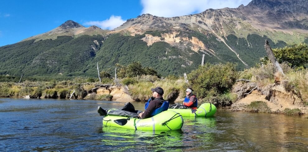 Dos turistas navegando en balsas de packrafting por las aguas cristalinas del Río Olivia, con la Cordillera de los Andes de fondo en Ushuaia. Excursión de Vértice Expediciones.