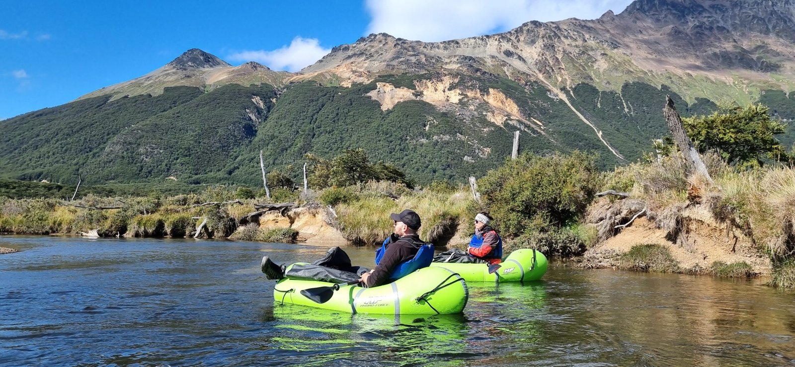 Dos turistas navegando en balsas de packrafting por las aguas cristalinas del Río Olivia, con la Cordillera de los Andes de fondo en Ushuaia. Excursión de Vértice Expediciones.