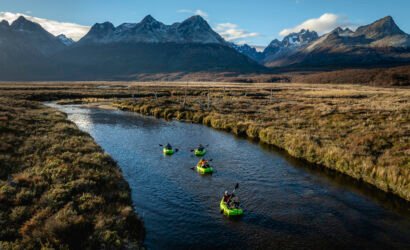 Grupo de personas navegando en packraft por el río olivia rodeado de montañas y un paisaje natural de la Patagonia bajo un cielo despejado - Vértice Expediciones