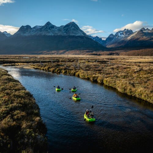 Grupo de personas navegando en packraft por el río olivia rodeado de montañas y un paisaje natural de la Patagonia bajo un cielo despejado - Vértice Expediciones