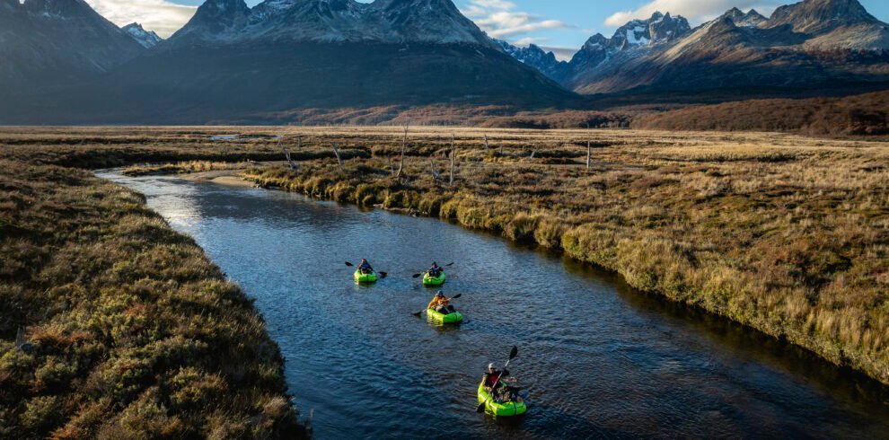 Grupo de personas navegando en packraft por el río olivia rodeado de montañas y un paisaje natural de la Patagonia bajo un cielo despejado - Vértice Expediciones