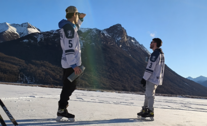 Dos patinadores en una laguna congelada de Ushuaia junto al guía Marcelo Vaca de Vértice Expediciones, con la cordillera de Tierra del Fuego de fondo y palos de hockey en primer plano.