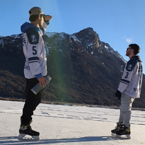 Dos patinadores en una laguna congelada de Ushuaia junto al guía Marcelo Vaca de Vértice Expediciones, con la cordillera de Tierra del Fuego de fondo y palos de hockey en primer plano.