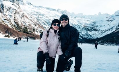 Pareja con ropa de montaña y lentes de sol posando sobre la nieve en Laguna Esmeralda con VERTICE EXPEDICIONES.