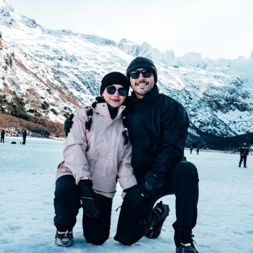 Pareja con ropa de montaña y lentes de sol posando sobre la nieve en Laguna Esmeralda con VERTICE EXPEDICIONES.