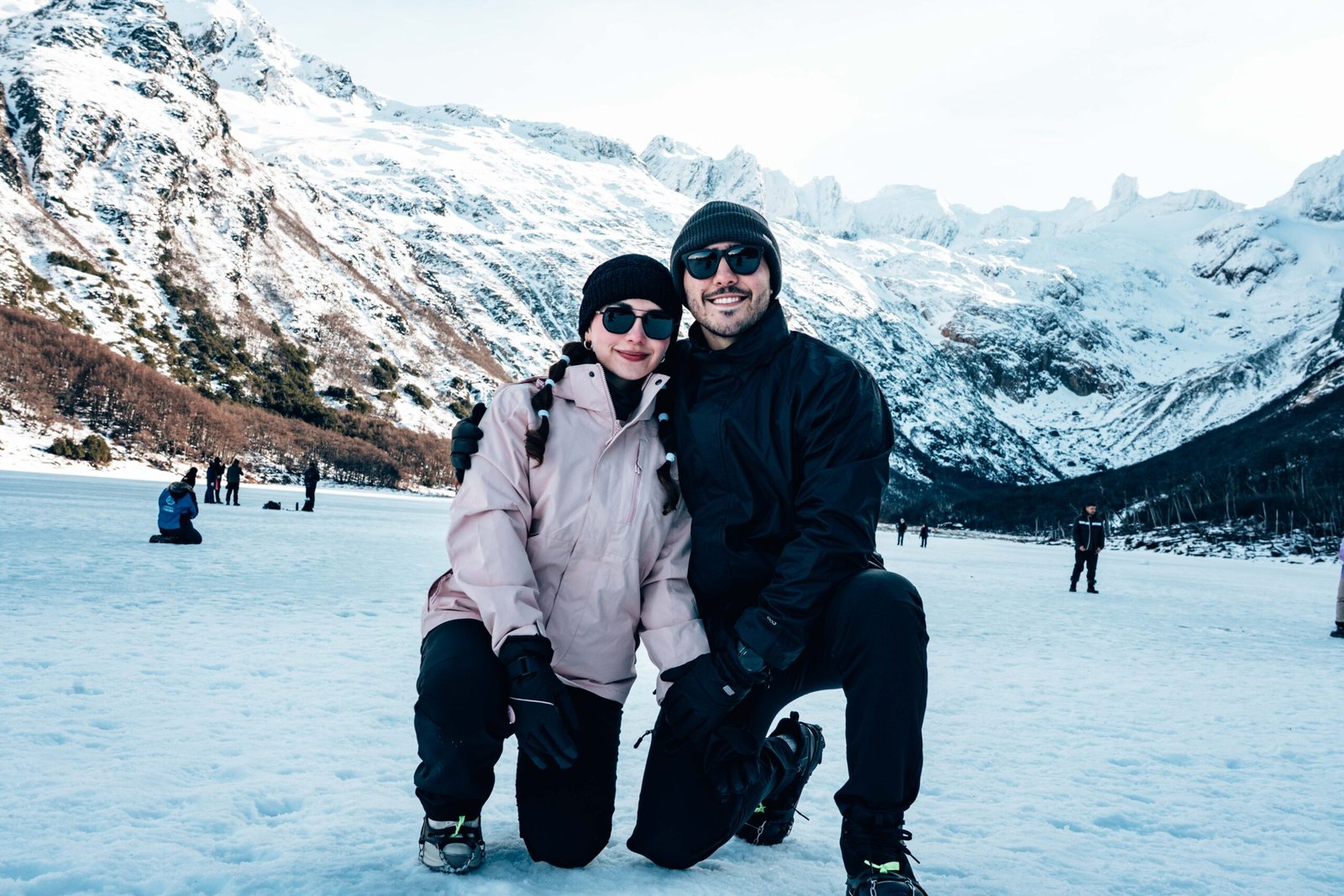 Pareja con ropa de montaña y lentes de sol posando sobre la nieve en Laguna Esmeralda con VERTICE EXPEDICIONES.