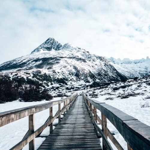 Puente peatonal de madera en perspectiva central sobre la nieve hacia la montaña con VERTICE Expediciones.