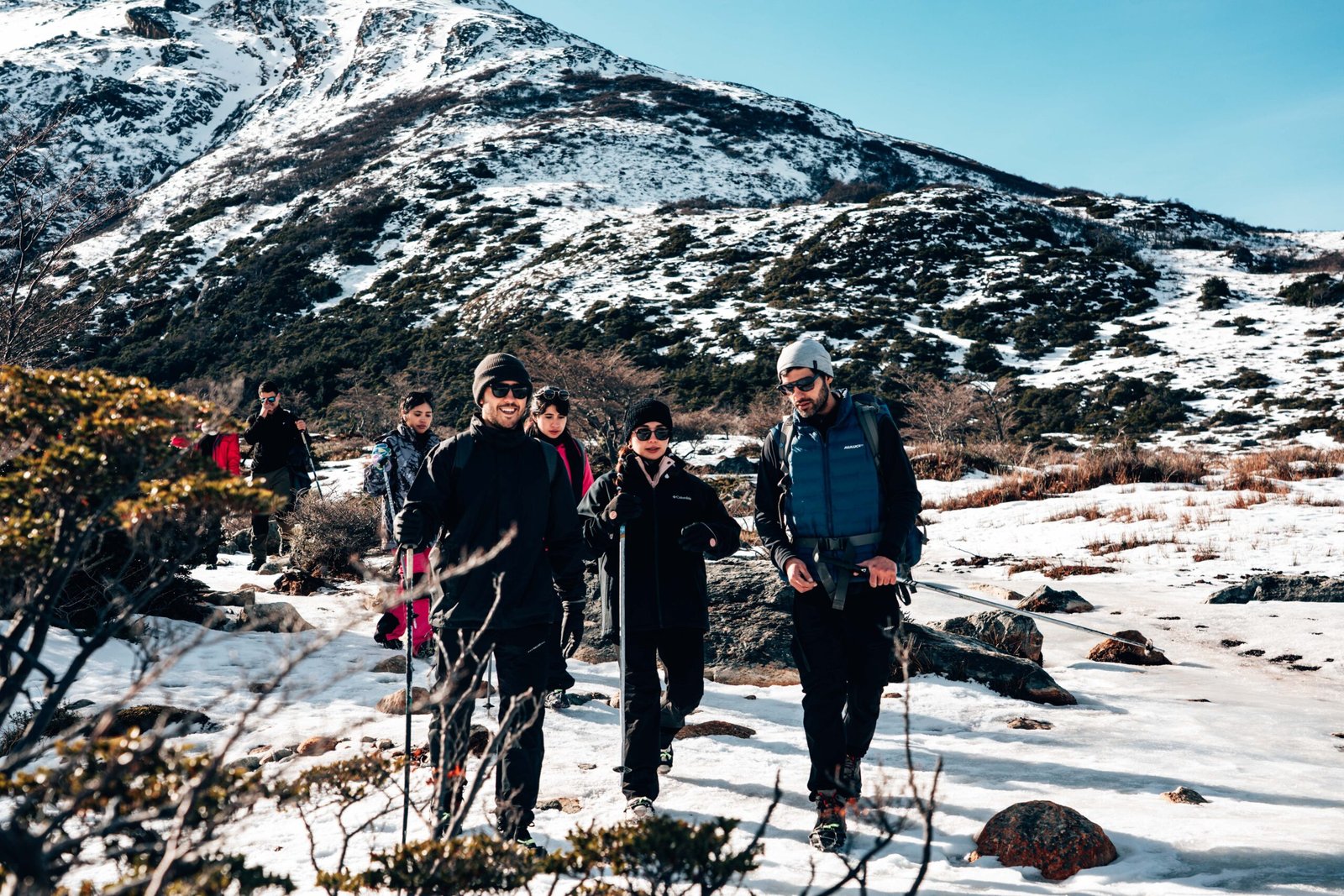 Grupo guiado por VERTICE caminando con bastones y ropa de abrigo por sendero nevado hacia Laguna Esmeralda Ushuaia