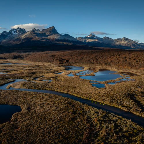 Grupo navegando en packraft por un río serpenteante rodeado de turbales y montañas en Tierra del Fuego con Vértice Expediciones.