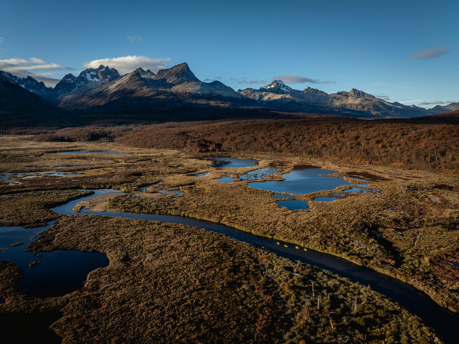 Grupo navegando en packraft por un río serpenteante rodeado de turbales y montañas en Tierra del Fuego con Vértice Expediciones.