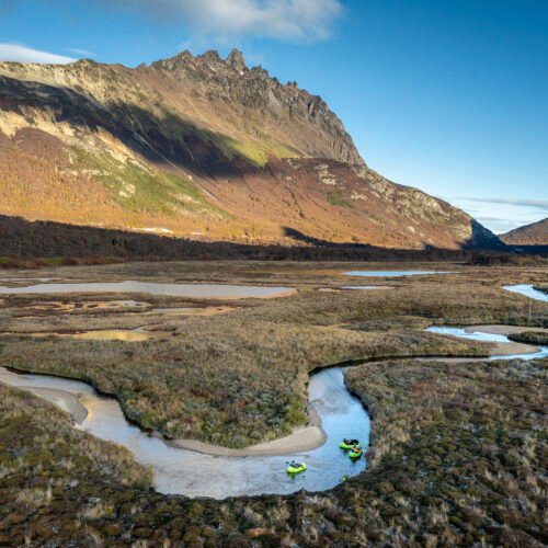 Aventureros en packrafts verdes remando en la curva de un río serpenteante al pie de una montaña en Ushuaia.
